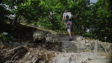 back shot young man walks hiking a mountain trail bare chest, snapback hat, mountaineer gear, climbing outdoors, looking around for a wall to climb, sunny summer weather in austria, durnstein, europe