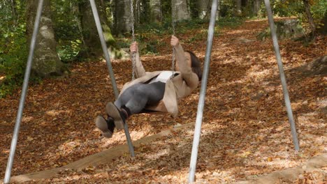 Smiling-young-woman-having-fun-on-swing-in-park-during-beautiful-autumn-day