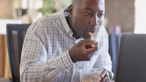 happy african american casual businessman using smartphone and having lunch in office, slow motion
