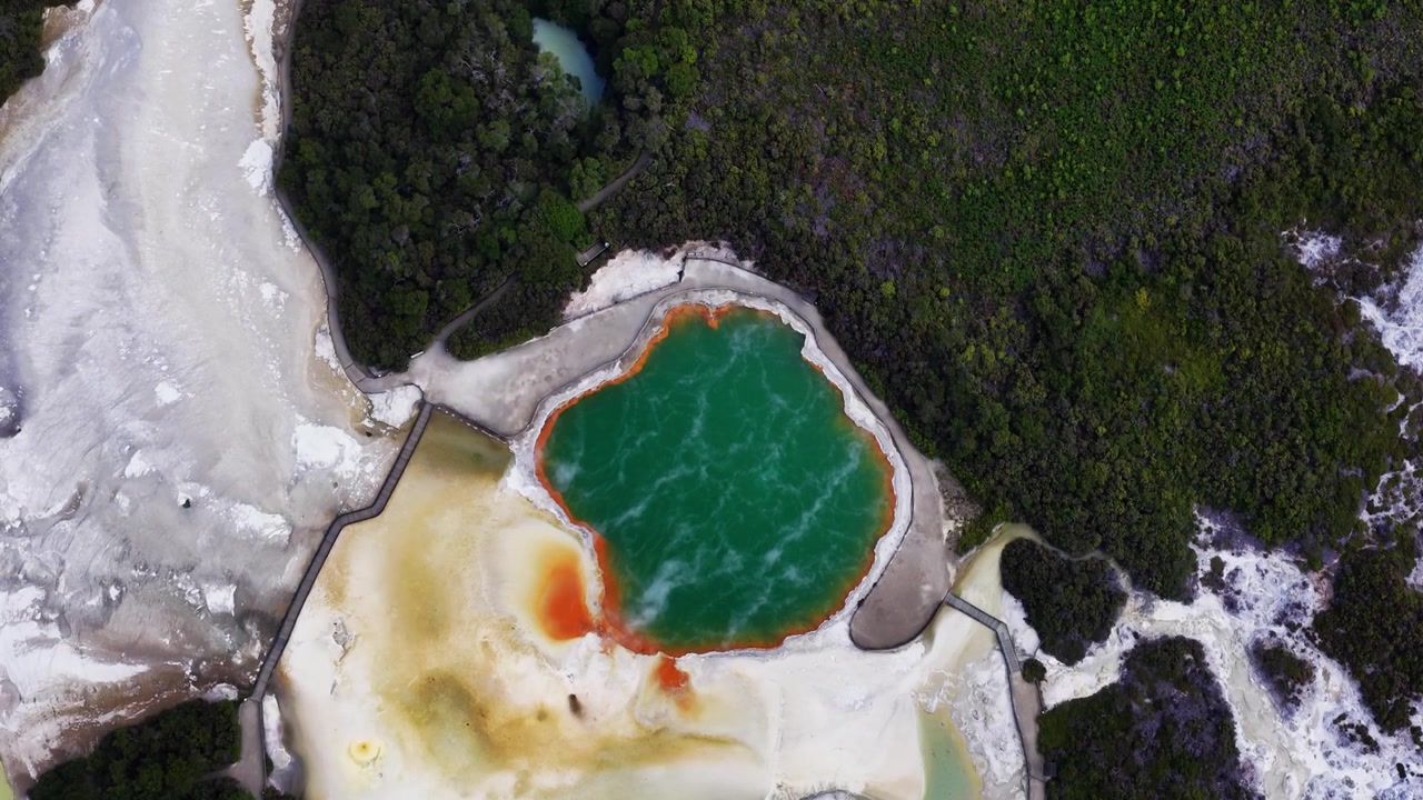 Jezírko Champagne, Rotorua, Bay of Plenty, Nový Zéland, letecký pohled shora na smaragdový geotermální horký pramen s oranžovým minerálním okrajem, sopečnou krajinu a původní les.