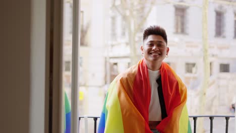 joyful person draped in rainbow pride flag on balcony