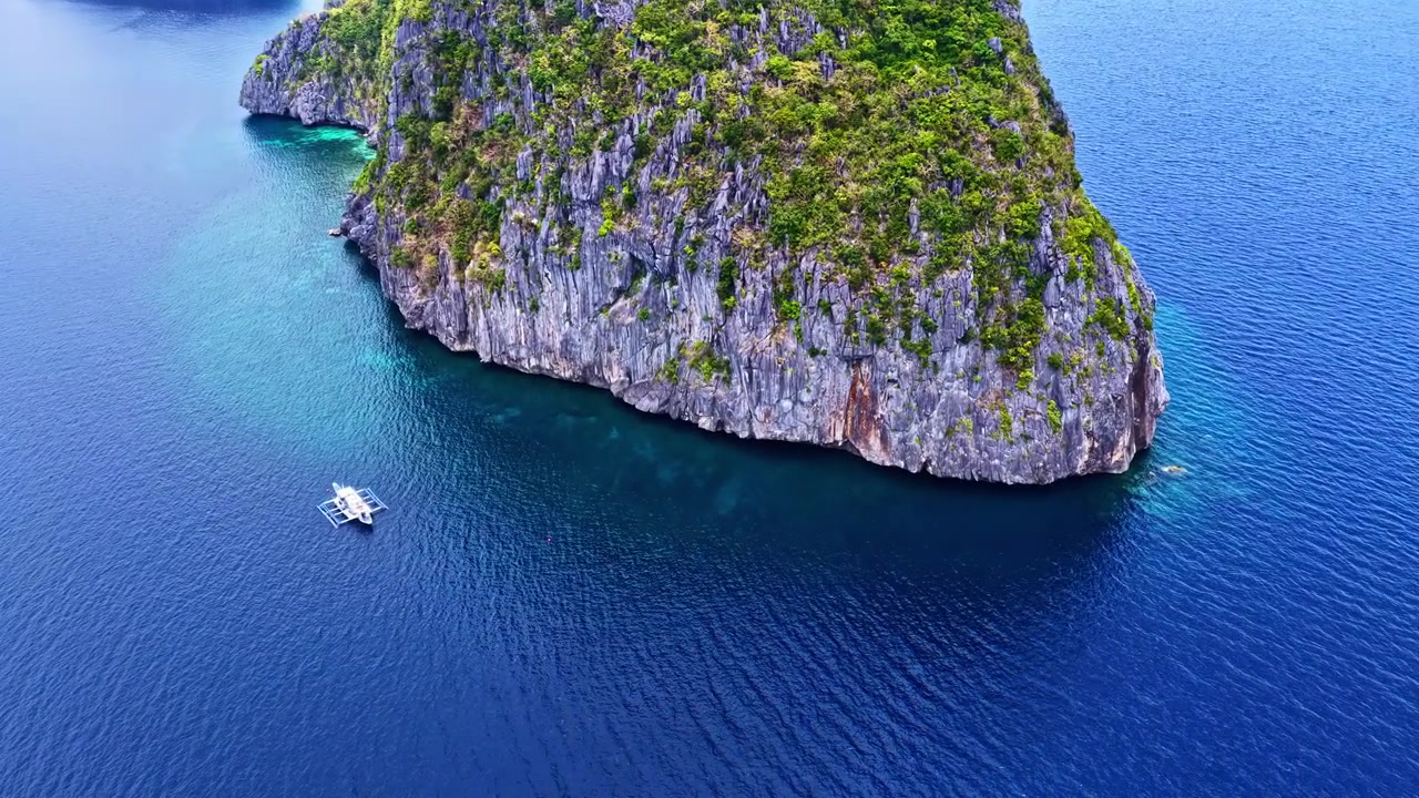 Spettacolare ripresa con drone su El Nido, Palawan, Filippine. Mostra un'enorme isola di scogliera calcarea che emerge dalle profonde acque blu dell'oceano accanto a una tradizionale barca a bilanciere in una giornata limpida.