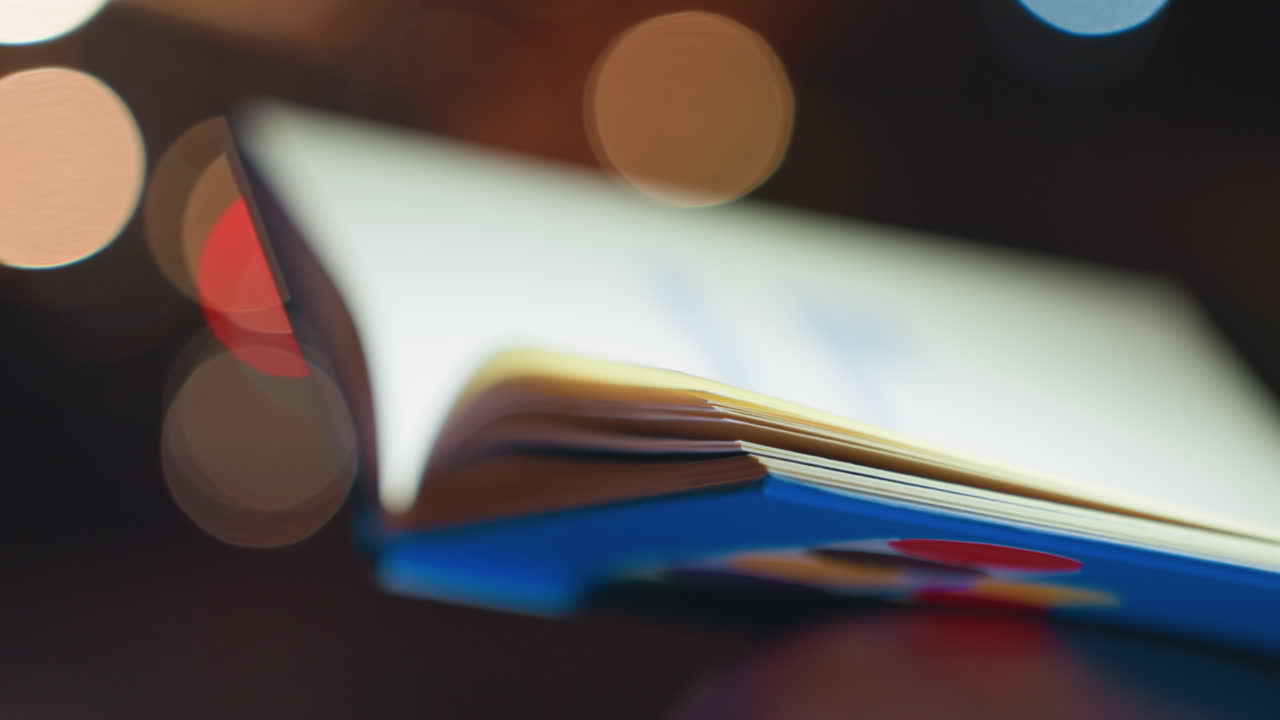 Shallow focus pages turning with bokeh, detailed edge and binding of illustrated book, glossy color shapes and soft blur, slow flip motion creating dreamy night mood and quiet wonder