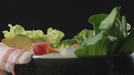 close up of a pot of shabu ingredients spinning around on the black background