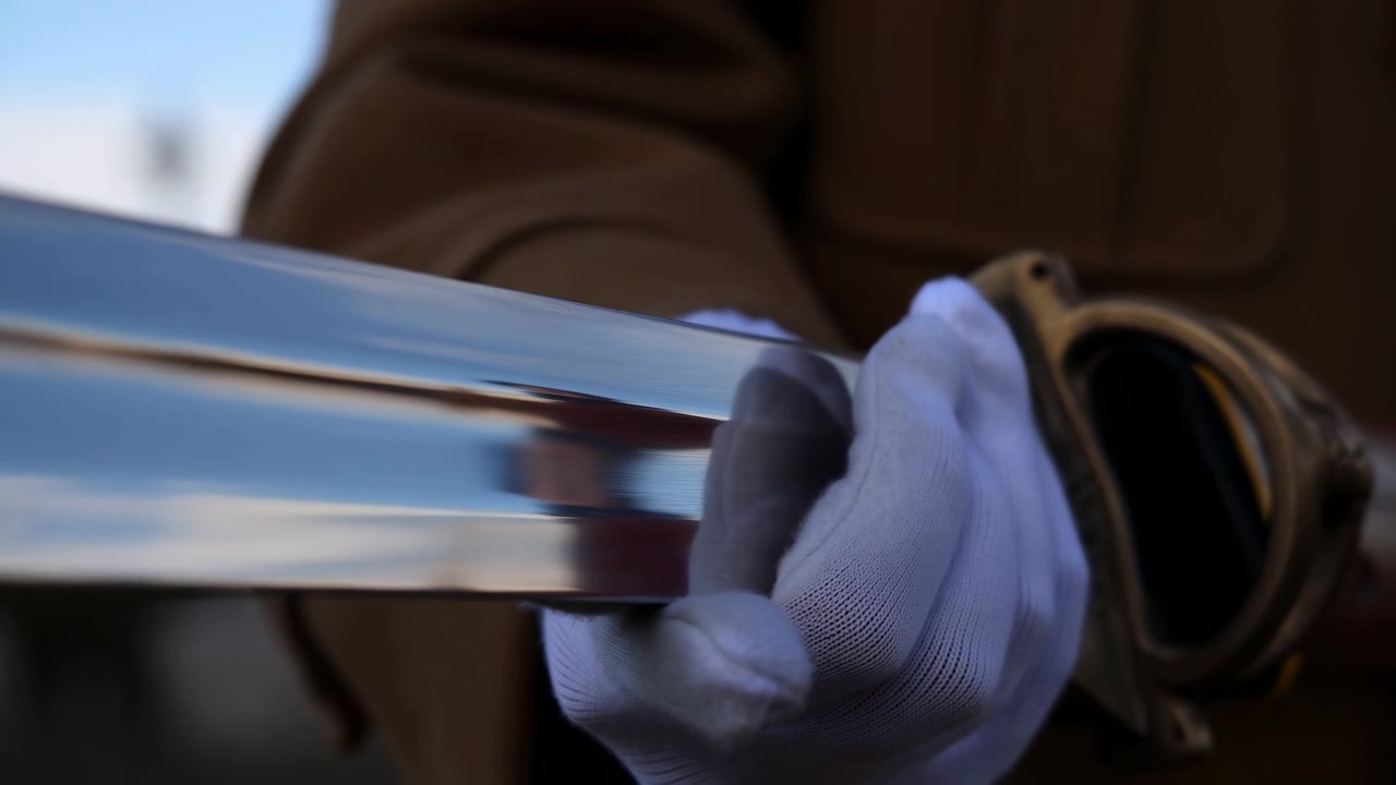 White gloved fingers move along smooth reflective metal tubes near a dark round fitting, while shallow focus and warm indoor light emphasize polished texture and careful handling.