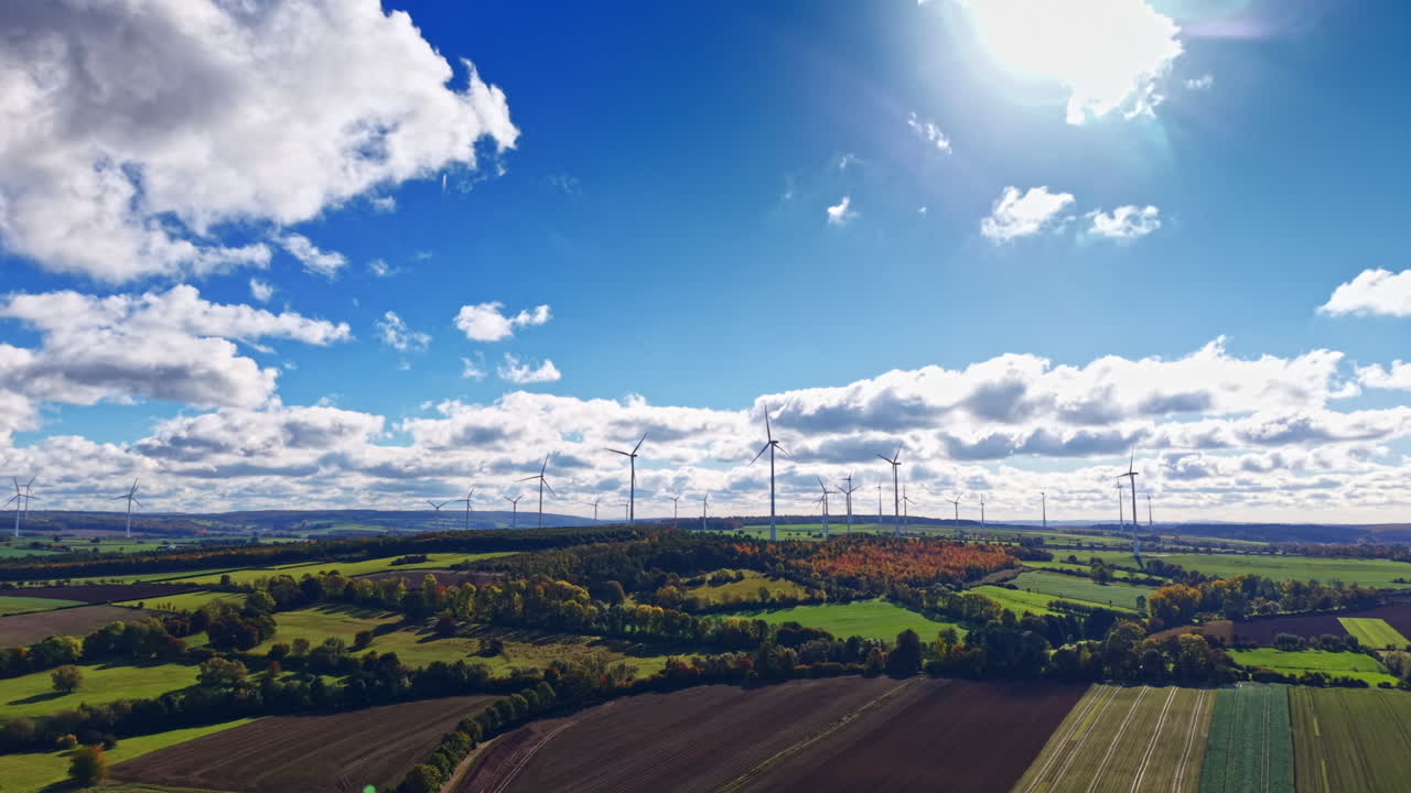 Le turbine eoliche si estendono in un vivace paesaggio sotto un cielo luminoso, pieno di nuvole soffici, a dimostrazione dell'armonia tra natura ed energia rinnovabile in un sereno contesto rurale