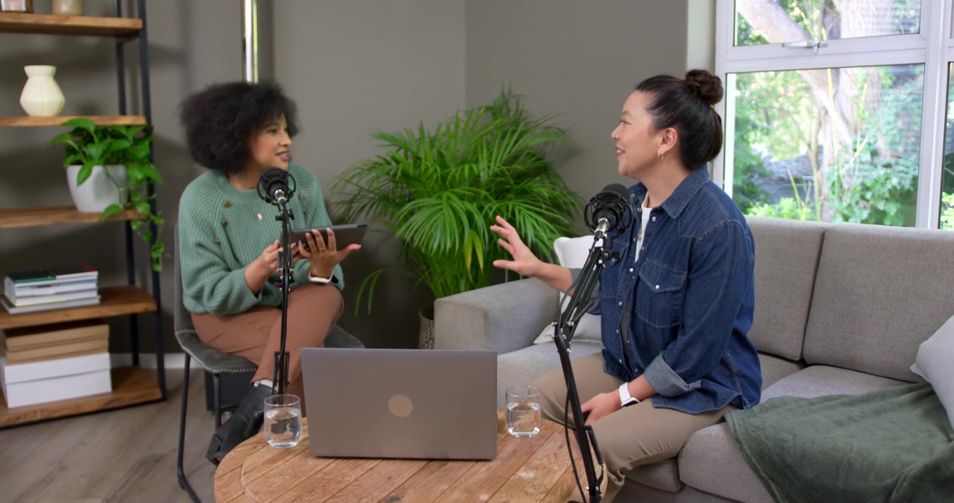Co-conduttrici diverse che leggono dal tablet per un podcast, parlando nei microfoni e gesticolando sopra il laptop.