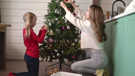 madre con su hija recogiendo adornos navideños de una caja y colgándolos en el árbol de navidad 1