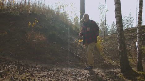 inspired middle-aged man with backpack is hiking alone in sunny forest at autumn day admiring wild nature travelling at native places