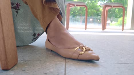 woman sitting on a chair with her feet in beige flat shoes with a gold chain