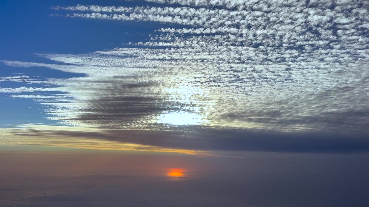 A left side cockpit view of a sunrise over the Mediterranean sea of a layer of parallel altocumulus clouds