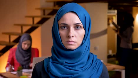 closeup portrait of adult beautiful muslim woman in blue hijab looking straight at camera being on the workplace indoors