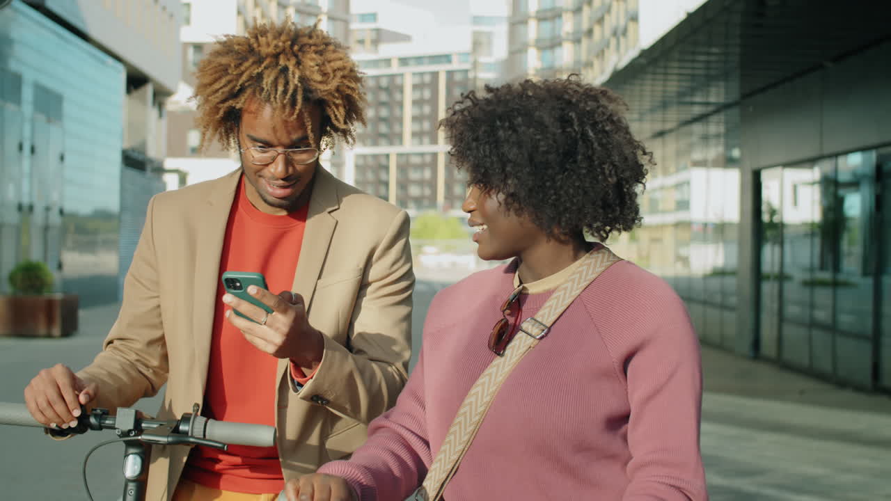amigos afroamericanos con scooters eléctricos usando el teléfono y hablando en la ciudad
