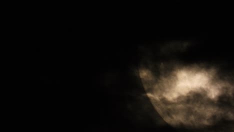 illuminated close-up of the moon in the dark sky with clouds passing by