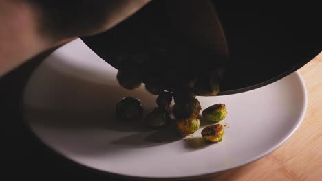 un primer plano de las coles de bruselas recién asadas que se sacan de una sartén caliente en un plato blanco, las verduras marinadas se convierten en un plato de acompañamiento sabroso y saludable