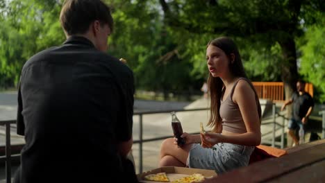 young couple hanging out at skatepark eating pizza and soda