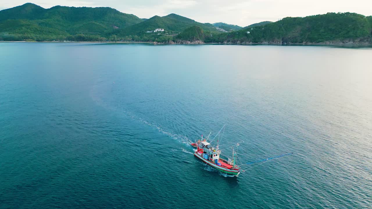 Lone fishing boat on open sea under a vast sky, captured from above as it moves through calm waters