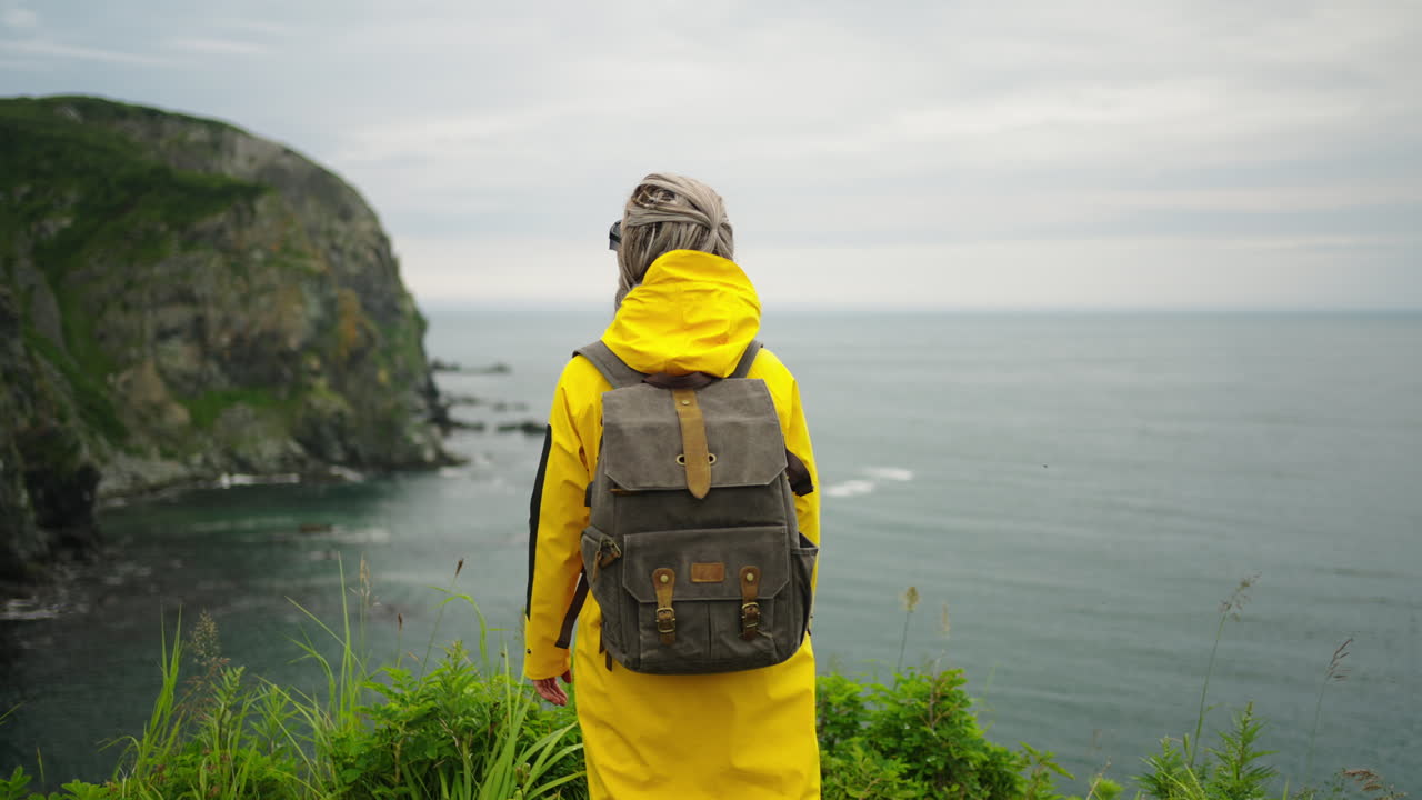 Woman Hiking on a Rocky Coastline in a Yellow Raincoat