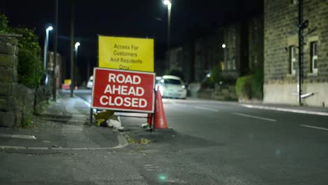 road closed sign with traffic passing by at night