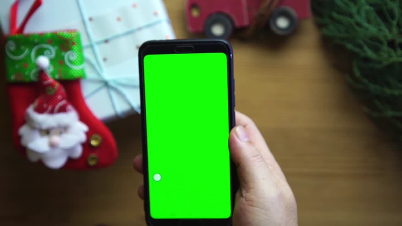 나무 배경 에 크리스마스 선물 에 대 한 녹색 화면 스마트 전화 를 들고 있는 사람