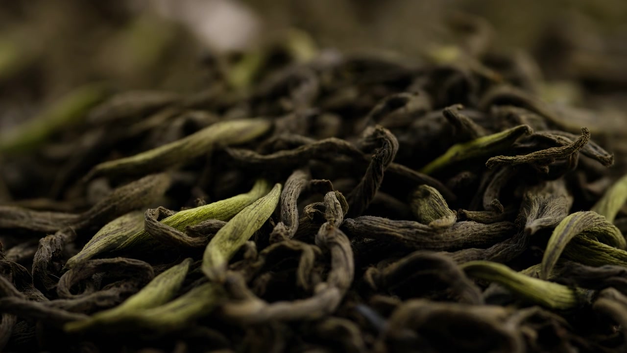 Macro movimento a livello degli occhi che mostra foglie di tè sfuse essiccate in un mucchio poco profondo, con le foglie centrali che rimangono nitide mentre le forme circostanti si ammorbidiscono, piccole punte si riallineano e un leggero assestamento aggiunge profondità.