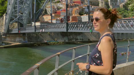 Red-haired-tourist-girl-taking-fotos-of-the-old-town-of-Porto-in-Portugal,-famous-Bridge-in-the-background