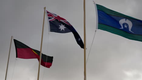 australian national flag, aboriginal flag and torres strait islander flag on a windy, overcast day