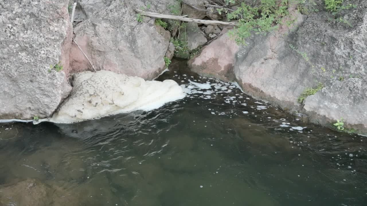 Polluted foam mixed with debris trapped between rocks in the riverbed
