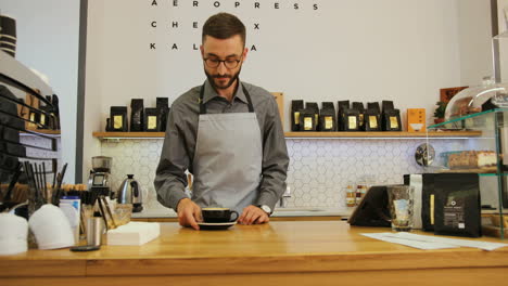 close-up view of male barista in coffee shop making a cup of coffee for the visitor and looking at the camera