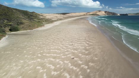 Group-of-people-walking-on-long-sandy-Te-Werahi-Beach,-Cape-Maria-van-Diemen