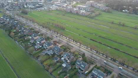 aerial of cars driving over a calm road near a row of houses in a rural area