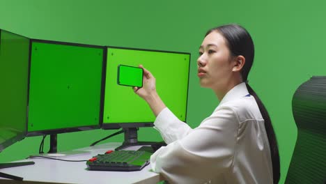 woman working at a computer with a green screen and a smartphone