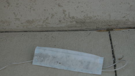 a dirty and used disposable face mask is dropped to the sidewalk