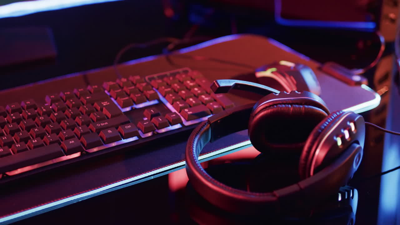 Video of computer gaming keyboard and gaming equipment on desk with copy space on neon background