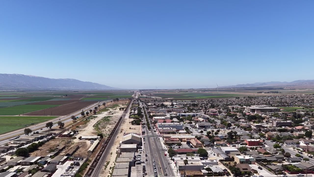 Drone video flying over Soledad, California, showcasing vibrant patchwork farmland, grid-like neighborhoods, mountains, and clear daylight. Perfect aerial footage for urban and rural contrasts.
