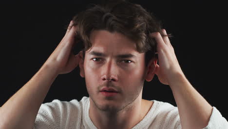 head and shoulders studio shot of unhappy man looking playing with hair in slow motion