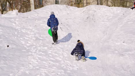 boys with plastic sleds on a slide in winter. back view of children on snow background. slow motion of boys rising up the snowy hill outdoors.