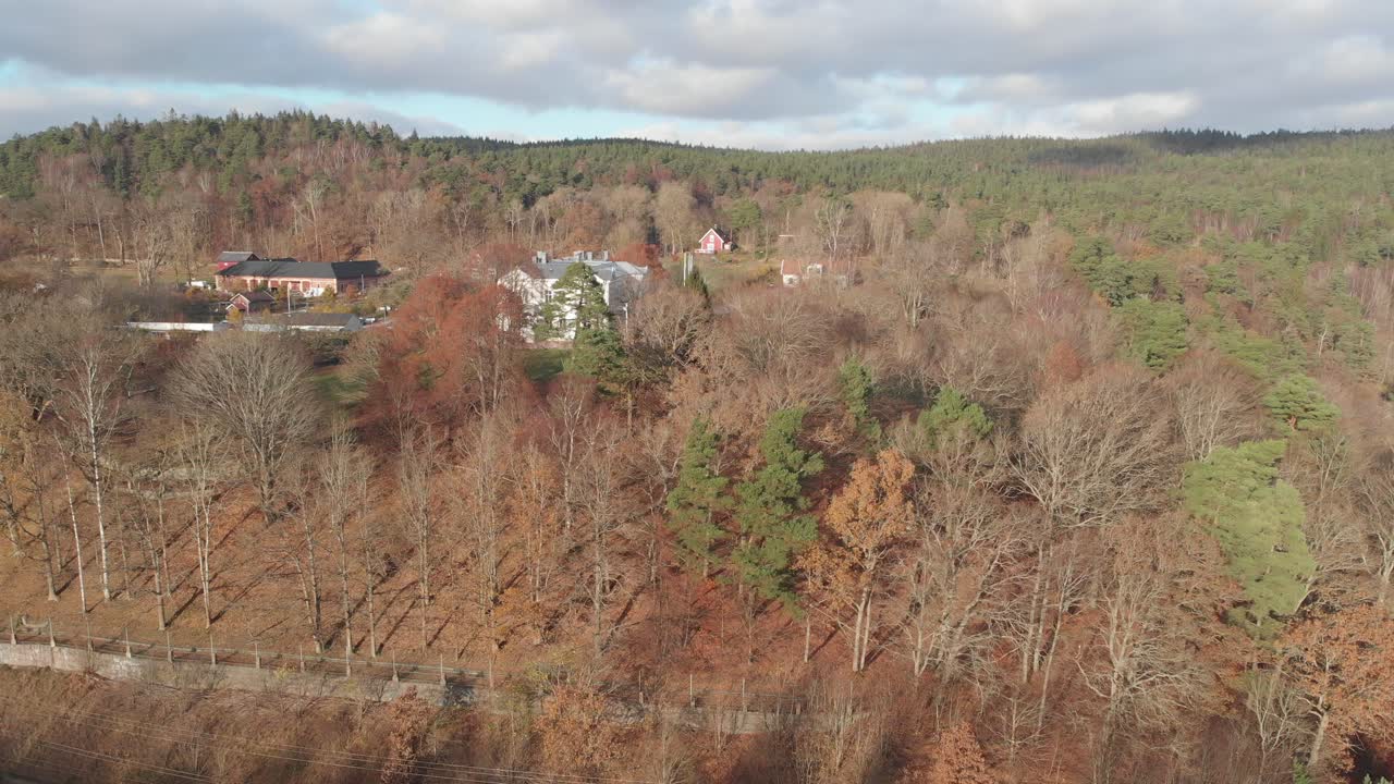 Drönare flyger över en höstskogsscen för att avslöja lantliga hus.