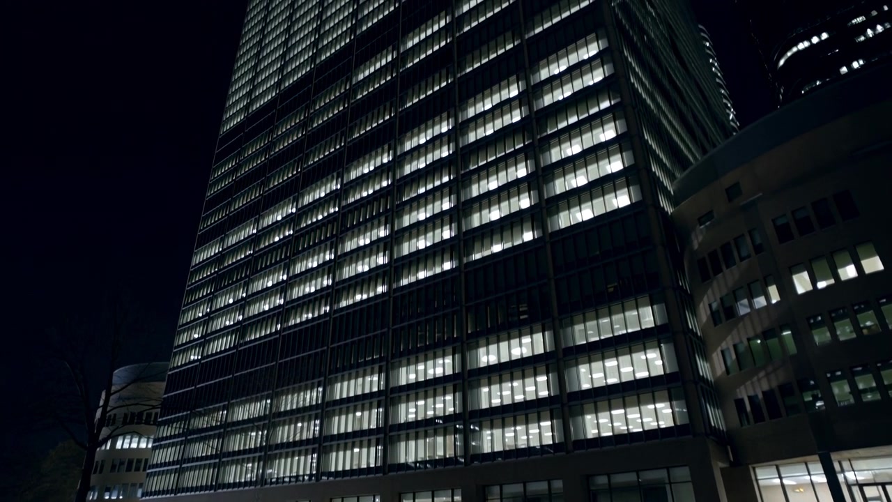 Uno splendido paesaggio urbano notturno con moderni grattacieli illuminati visti dall'alto, che mostrano le eleganti facciate in vetro e metallo che creano un ambiente urbano drammatico e sereno.