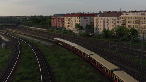 Tracking-Ansicht-Des-S-Bahn-Zugs,-Der-In-Den-Bahnhof-Unter-Der-Bosebrucke-Brücke-Einfährt.-Luftaufnahme-Der-Mehrgleisigen-Eisenbahnstrecke.-Stadtszene-In-Abendlicher-Holden-Stunde.-Berlin,-Deutschland