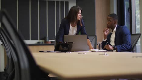 diverse businessman and businesswoman discussing and using laptop in modern office