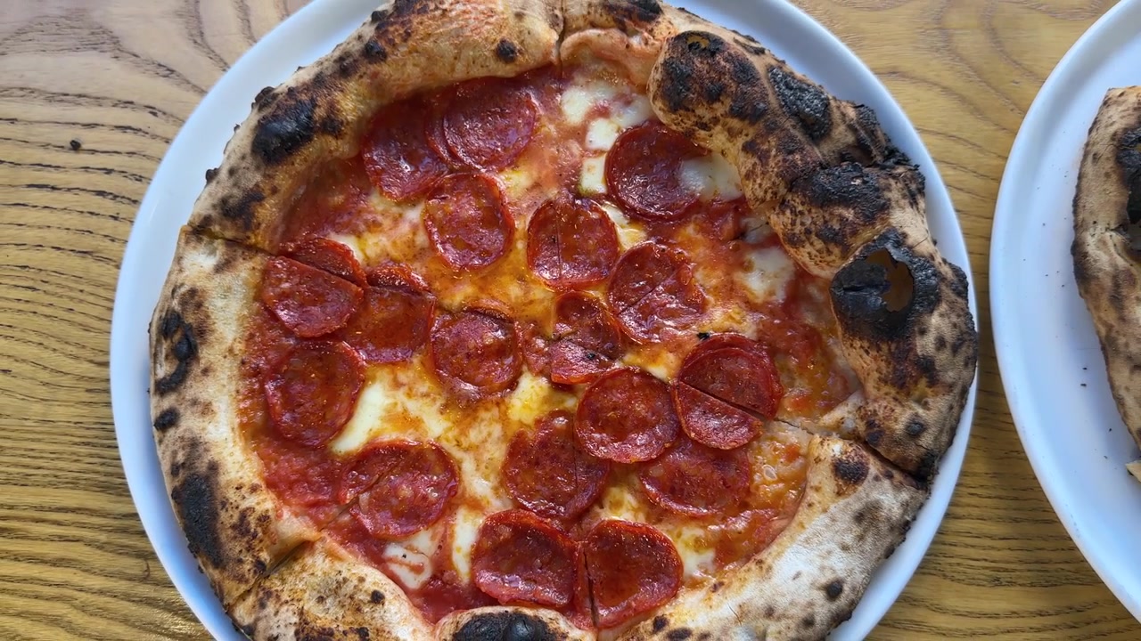 Zoom indietro dall'alto di una pizza fresca al salame piccante con mozzarella fusa su un tavolo di legno