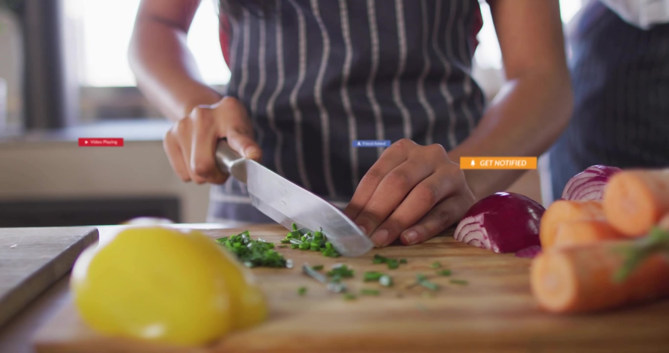 Adolescente che cucina tritando erbe in cucina, con badge dell'interfaccia utente che fluttuano mentre un genitore guida una lezione di cucina.
