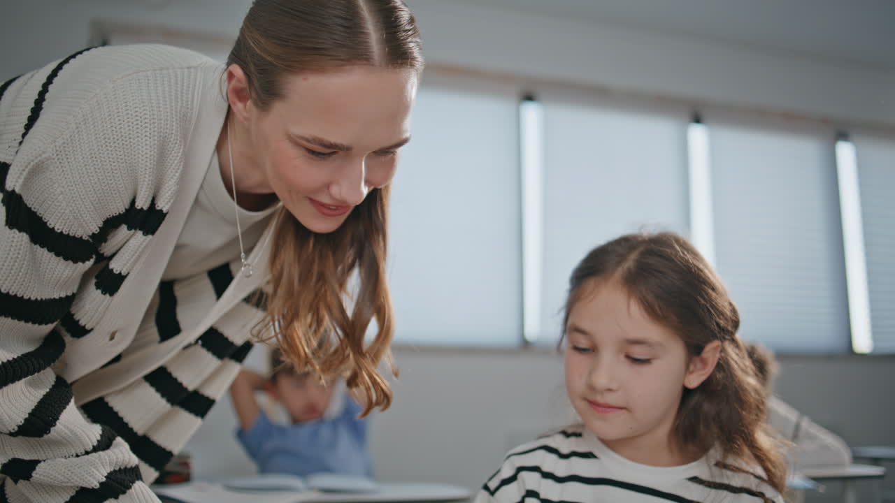Girl listening woman teacher in light classroom closeup. Schoolteacher helping