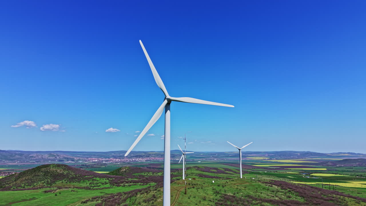 Wind turbines stand tall on rolling hills with a clear blue sky during the daytime in a rural area