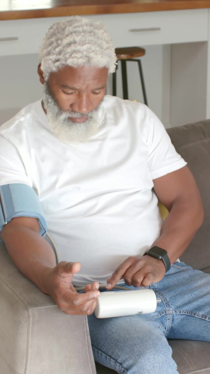 Video verticale: Uomo maturo seduto che tocca un monitor bianco dopo aver applicato il bracciale a casa, controllando la pressione sanguigna.