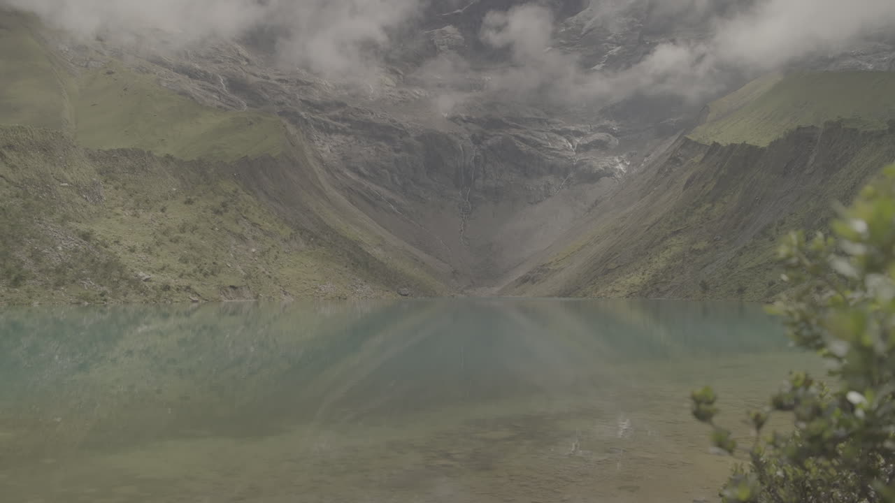 Tilting up shot of Humantay Lake Peru with clouds near the mountain reflecting on the clear blue water LOG