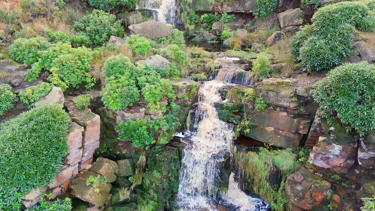 Yorkshire Moors' wondrous waterfall, aerial footage displays water flowing over large rocks into a deep blue pool, hikers at the bottom