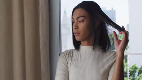 Mixed-race-gender-fluid-person-looking-through-window-at-home