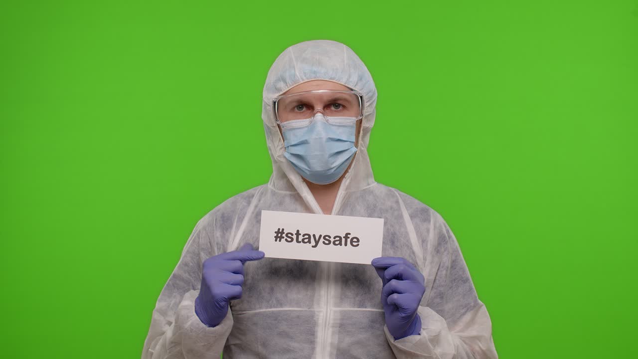 보호복을 입은 남자가 '안전하게 지내라'는 표지판을 들고 있다